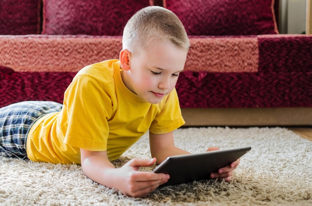 Foto alumno estudiando en casa con tableta digital en la mano y haciendo la tarea escolar