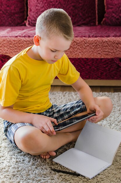 Alumno estudiando en casa con tableta digital en la mano y haciendo la tarea escolar