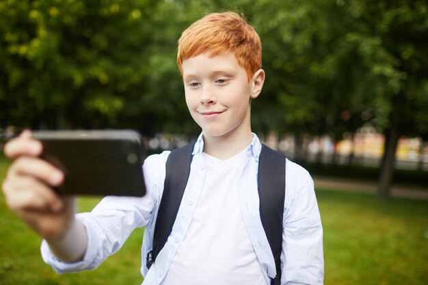 Alumno masculino moderno tomando selfie en el parque