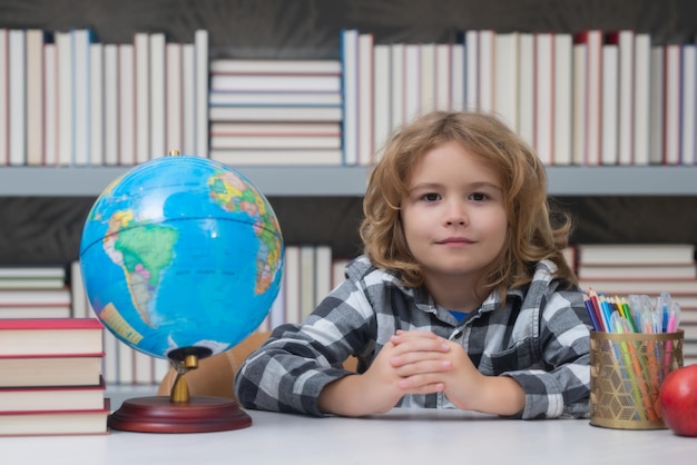 Foto alumno mirando el mundo en la biblioteca de la escuela primaria regreso a la escuela retrato de niño lindo niño escolar niño inteligente con útiles escolares