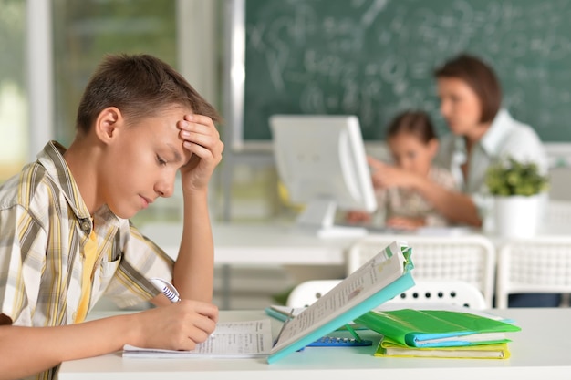 Alumno que estudia lecciones en la clase de informática con el profesor y el alumno borrosa en el fondo