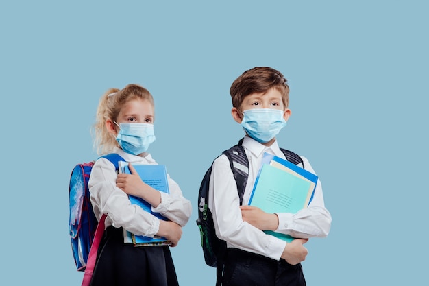 Alumno de regreso a la escuela con máscara médica y mochila tiene cuadernos y libros en la mano aislados o ...