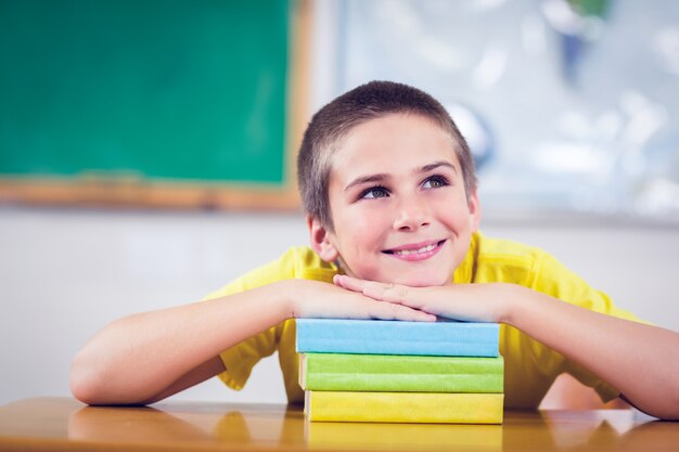 Alumno sonriente que se inclina en la pila de libros en una sala de clase