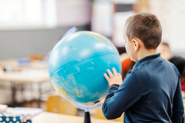 Foto un alumno tratando de encontrar un país en un globo terráqueo en clase de geografía