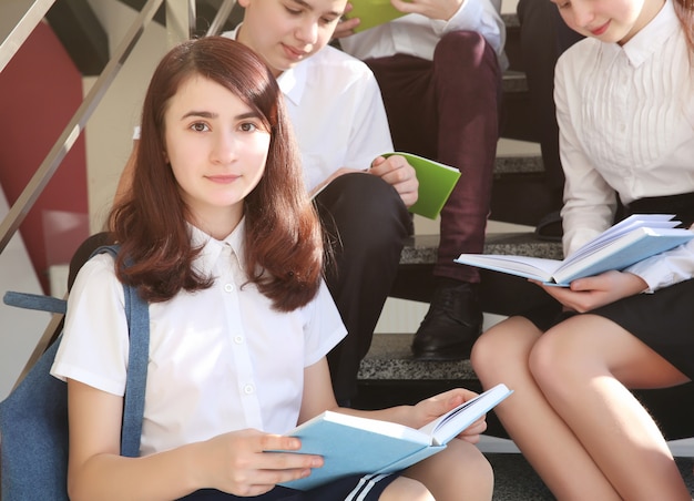 Alumnos felices con libros sentados en las escaleras de la escuela