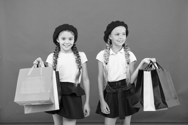 Alumnos de los niños satisfechos con las compras de fondo rojo Obsesionados con los centros comerciales y de ropa Concepto de adicto a las compras Señales de que eres adicto a las compras Los niños lindas colegialas sostienen bolsas de compras