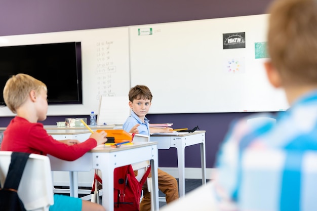 Alumnos de primaria caucásicos sentados frente a un escritorio en el aula