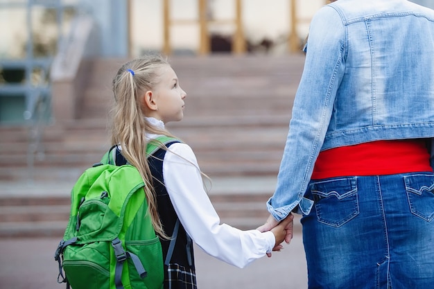 Aluna adolescente de uniforme com uma mochila na mão com a mãe, caminha pela escada para a escola. Vista traseira.