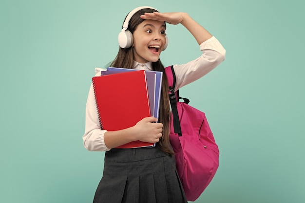 Aluna adolescente em fones de ouvido segura livros sobre fundo de estúdio isolado azul Escola e conceito de educação musical De volta à escola