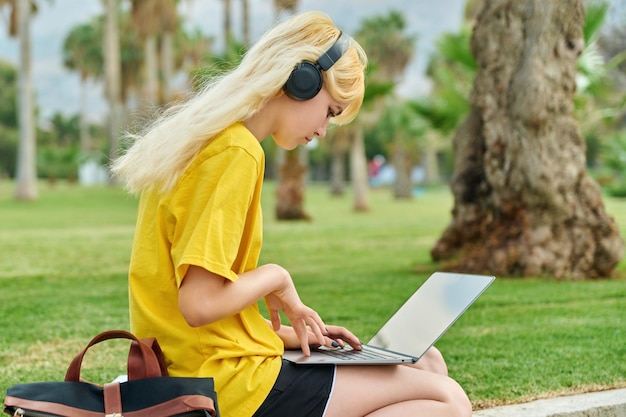 Aluna adolescente em fones de ouvido sentado no parque com laptop