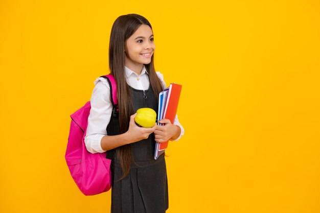 Aluna adolescente em idade escolar com mochila escolar segura aplle e livros sobre fundo de estúdio isolado amarelo Escola infantil e conceito de educação