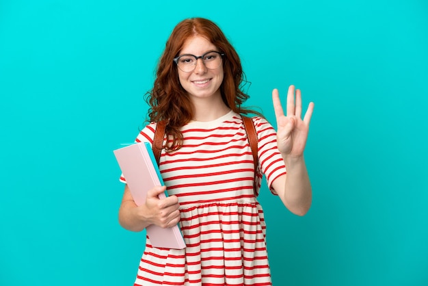 Aluna adolescente ruiva isolada em um fundo azul feliz e contando quatro com os dedos