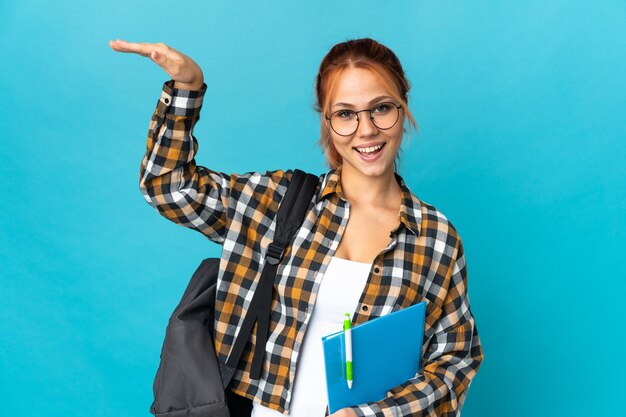 Aluna adolescente russa isolada em uma parede azul segurando copyspace para inserir um anúncio