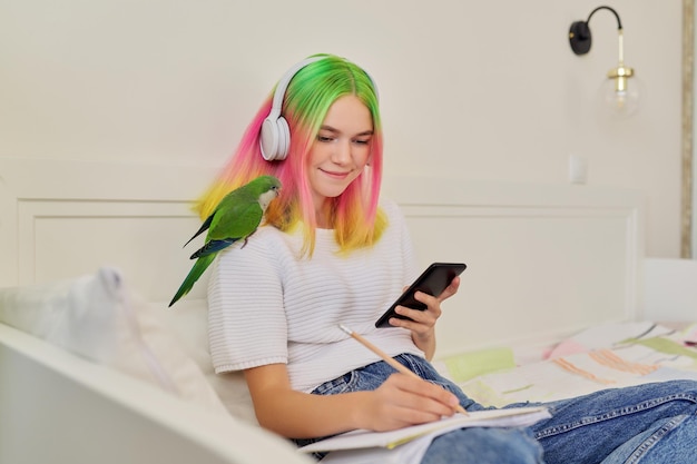 Aluna adolescente sentada em casa na cama com papagaio de estimação no ombro