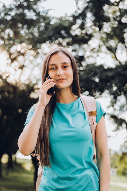 Aluna adolescente vestindo camiseta azul-marinho, fazendo um telefonema para o namorado no parque