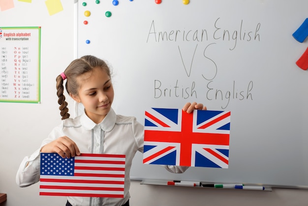 Aluna alegre com bandeiras americanas e britânicas na sala de aula, aprendendo diferenças nos tipos de idiomas