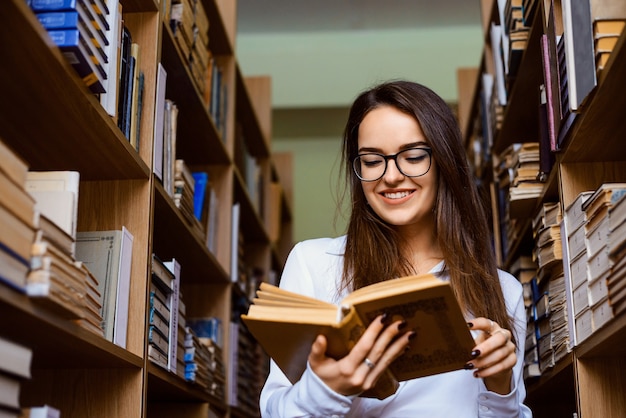 Aluna alegre parada entre estantes lendo um livro