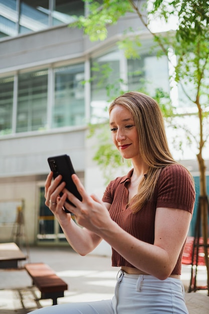 Aluna alegre usando seu telefone inteligente para verificar as mídias sociais durante um intervalo das aulas