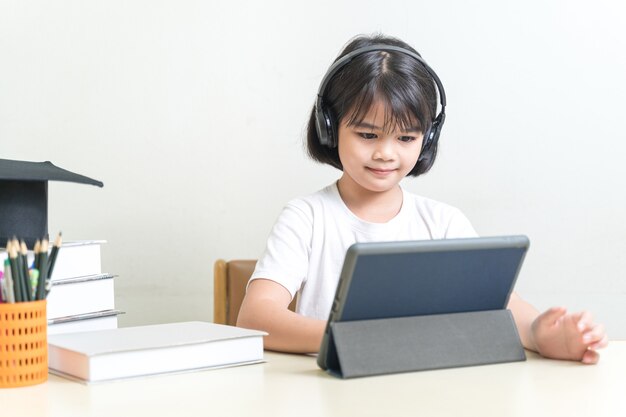 Aluna asiática alegre usando fone de ouvido, escrevendo no tablet digital para estudar em casa