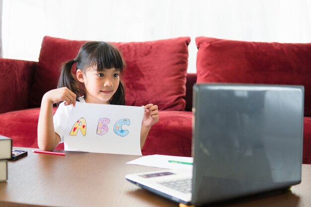 Aluna asiática de aprendizagem on-line com o laptop em casa.