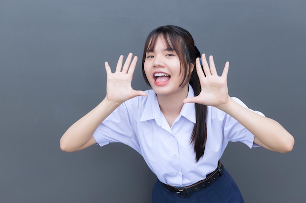 Aluna asiática do ensino médio em uniforme escolar com sorrisos confiantes com cinza ao fundo