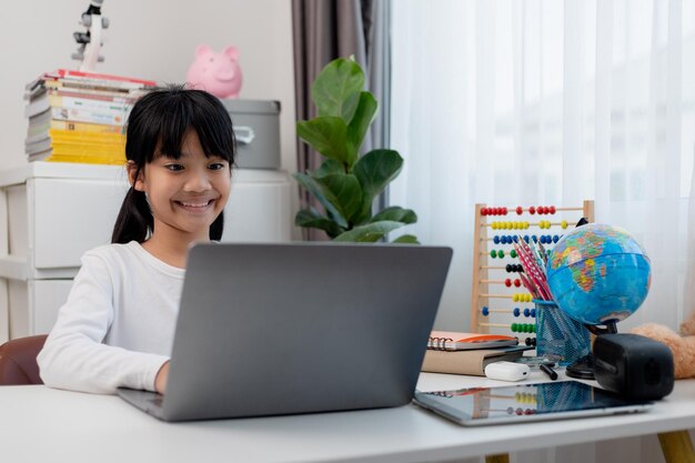 Aluna asiática fazendo lição de casa com laptop em casa Crianças usam gadgets para estudar Educação e ensino a distância para crianças Educação em casa durante a quarentena Fique em casa