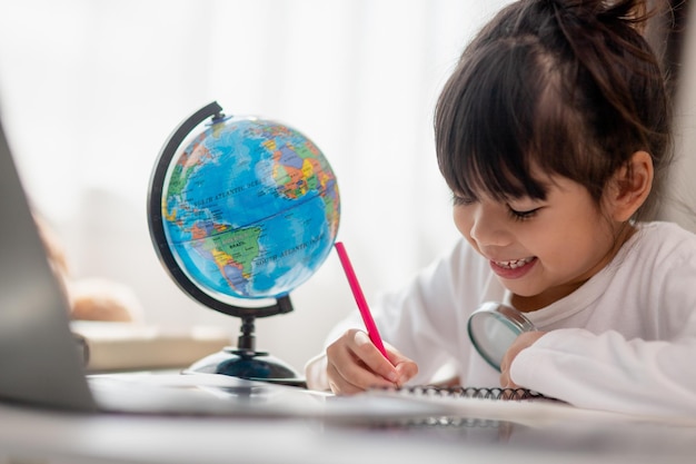 Aluna asiática fazendo lição de casa com laptop em casa Crianças usam gadgets para estudar Educação e ensino a distância para crianças Educação em casa durante a quarentena Fique em casa