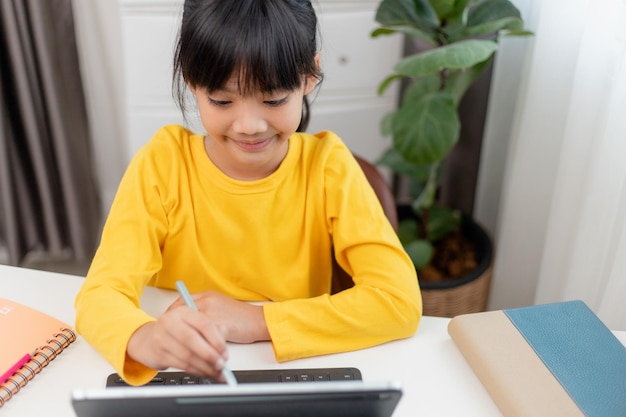 Aluna asiática fazendo lição de casa com tablet digital em casa Crianças usam gadgets para estudar Educação e ensino à distância para crianças Educação em casa durante a quarentena Fique em casa