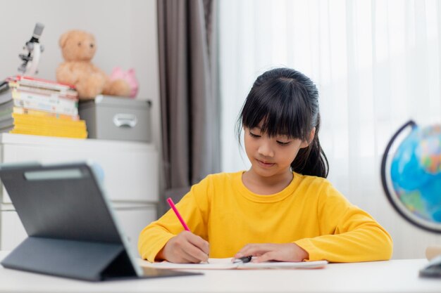 Aluna asiática fazendo lição de casa com tablet digital em casa Crianças usam gadgets para estudar Educação e ensino à distância para crianças Educação em casa durante a quarentena Fique em casa