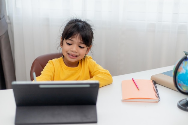 Aluna asiática fazendo lição de casa com tablet digital em casa Crianças usam gadgets para estudar Educação e ensino à distância para crianças Educação em casa durante a quarentena Fique em casa