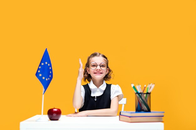 Aluna caucasiana levantando a mão sentada na mesa durante a aula, aula de inglês, bandeira da europa