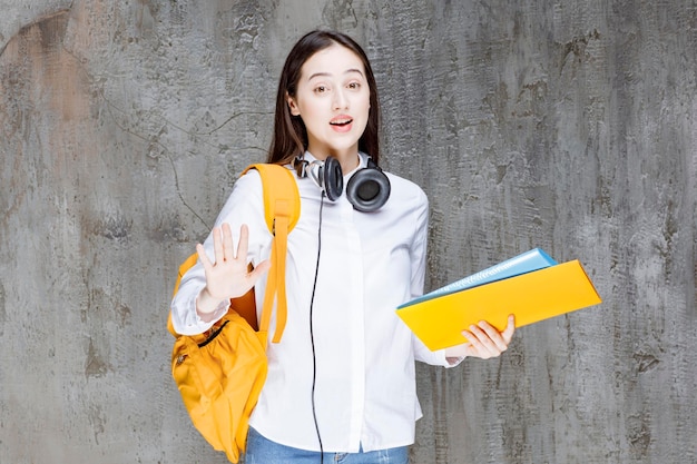 Aluna com mochila amarela e fones de ouvido em pé com o livro. Foto de alta qualidade