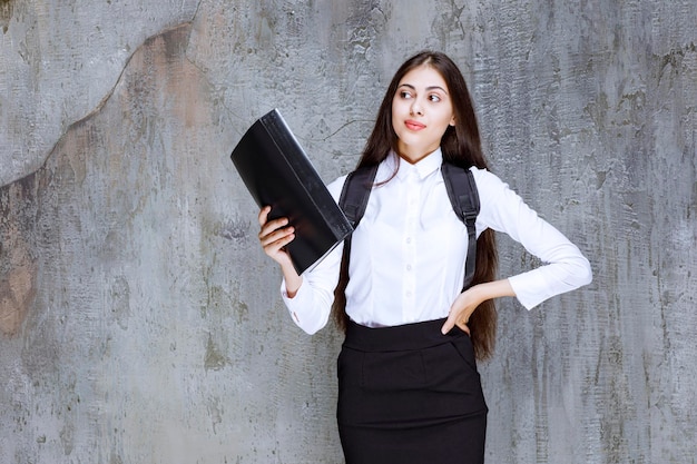 Aluna com roupa de escola segurando o livro sobre cinza. foto de alta qualidade