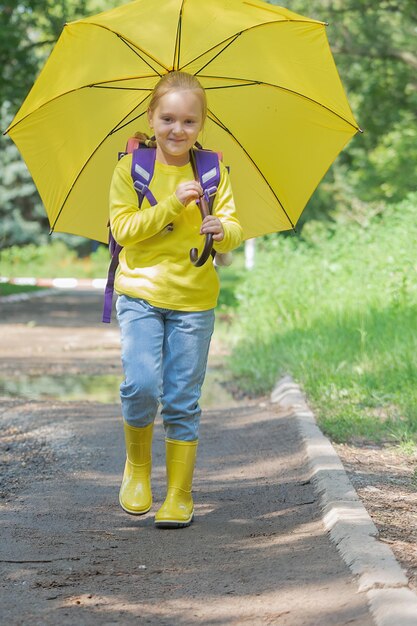 Aluna da escola primária vai para a escola com uma mochila e sob um guarda-chuva