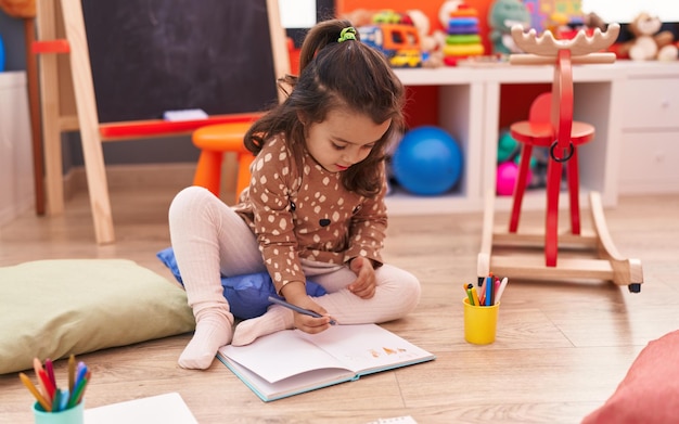 Aluna da pré-escola adorável garota hispânica sentada no chão desenhando no notebook no jardim de infância