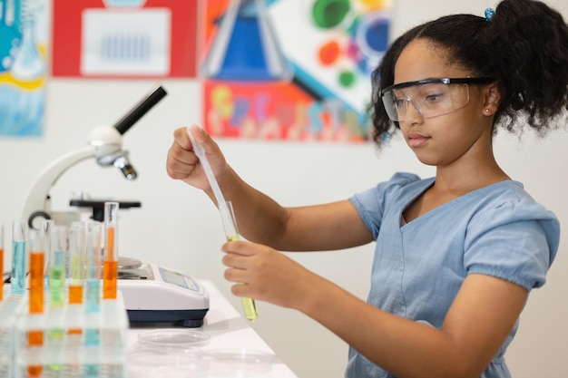 Foto aluna de escola primária biracial usando óculos de proteção fazendo uma experiência química em laboratório