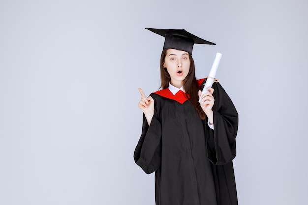 Aluna de pós-graduação em vestido com certificado de faculdade em pé. Foto de alta qualidade