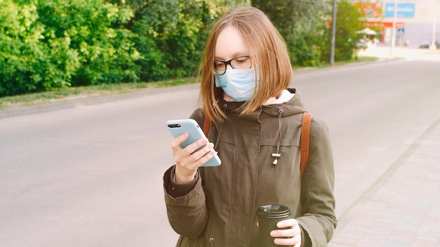 Aluna em uma máscara médica protetora e óculos escreve uma mensagem de texto lê notícias navega na Internet