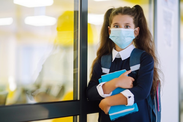 Aluna em uma máscara protetora com uma mochila e um livro didático