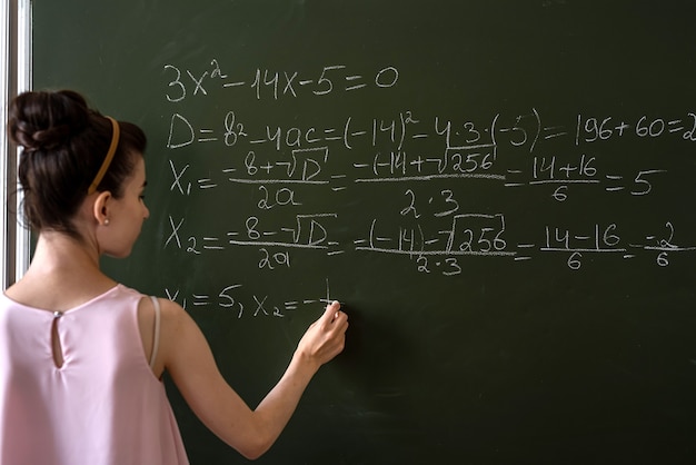 Aluna escrevendo fórmula matemática do ensino médio com giz no quadro-negro, álgebra da aula de matemática