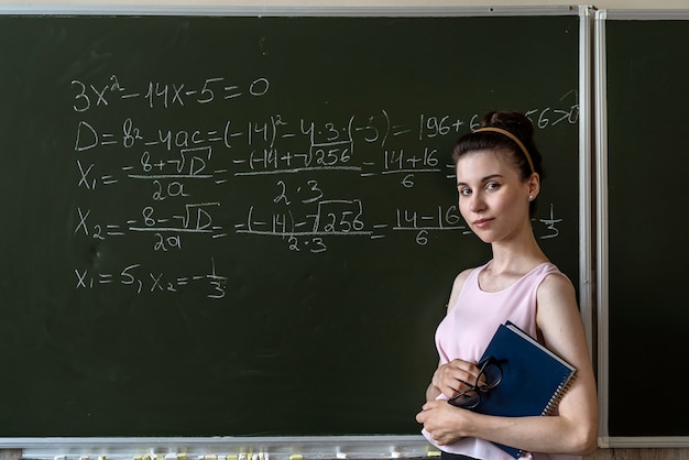 Aluna escrevendo fórmula matemática do ensino médio com giz no quadro-negro, álgebra da aula de matemática