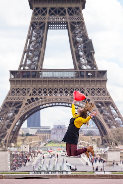 Aluna feliz e sorridente com um balão em forma de coração salta ao fundo da Torre Eiffel em Paris. França