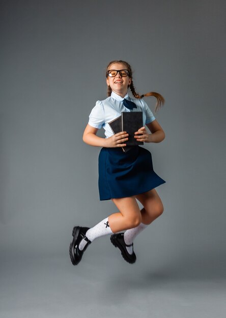 Aluna feliz em pé com um livro nas mãos, isolado em um fundo cinza