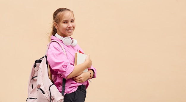 Foto aluna feliz em uma camisa fúcsia com uma mochila e livros em um fundo de pêssego