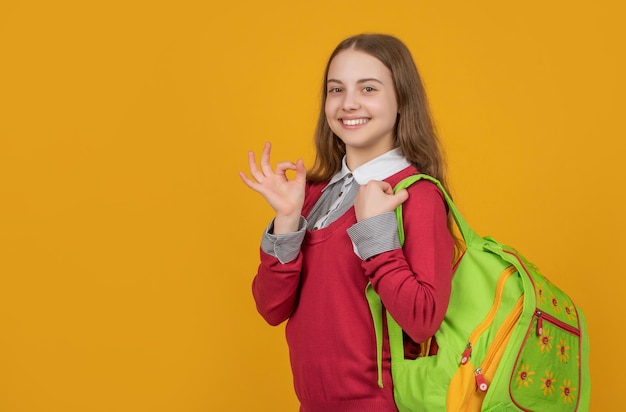 Aluna feliz mostrando gesto de anel OK carregando bolsa escolar fundo vermelho 1º de setembro