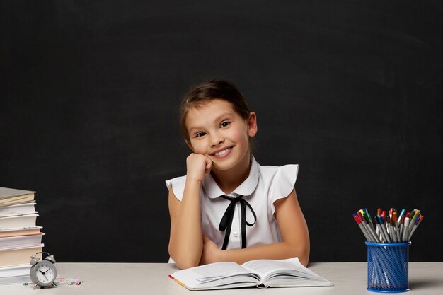 Aluna feliz sonhando acordada e sentado à mesa da sala de aula no fundo do quadro-negro. De volta à escola.