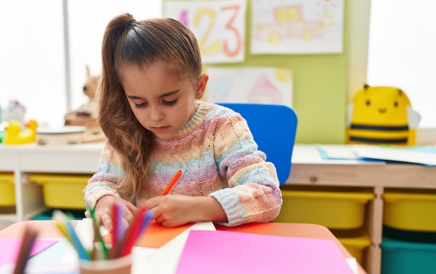 Aluna hispânica adorável sentada na mesa desenhando no papel no jardim de infância
