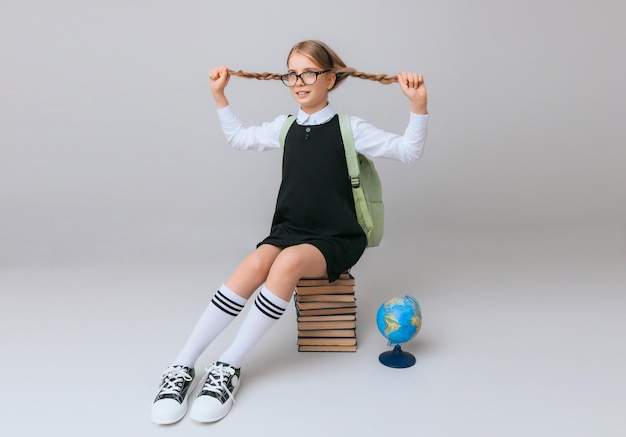 Aluna isolada em fundo amarelo com globo menina em uniforme escolar sentado em um fundo amarelo lendo um livro menina loira em uniforme escolar em um fundo amarelo