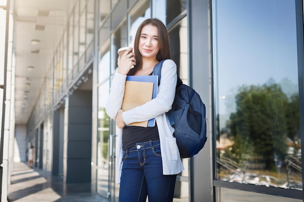 Aluna jovem, com livros e mochila. Ficar do lado de fora antes da aula e tomando café. Pensando no próximo dia. Conceito de estilo de vida e educação