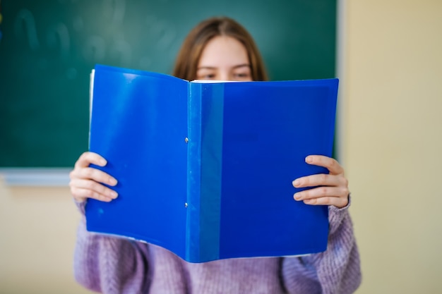 Aluna lendo notas da pasta azul. Segurando notas na frente do rosto.